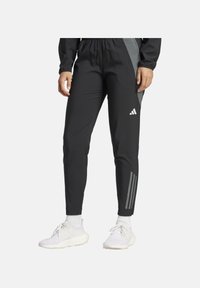 Schwarze Sporthose mit elastischem Bund, ausgestattet mit einem grauen Seitenpaneel und drei weißen Streifen am Unterschenkel. Hergestellt aus leichtem Material.