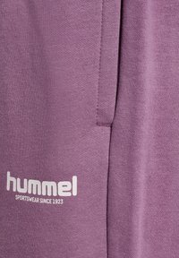 Lilla joggingbukser lavet af bomuldsblanding med en glat tekstur, sidelomme og hvidt "hummel"-logo med teksten "SPORTSWEAR SINCE 1923".
