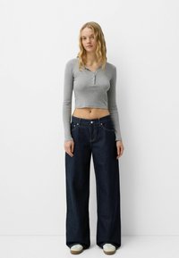 Gray long-sleeve cropped top with a buttoned neckline, paired with wide-leg dark blue denim jeans featuring prominent stitching and side pockets.