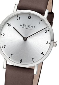 Montre analogique argentée avec un cadran brossé, des index horaires noirs et un bracelet en cuir marron. Présente un design minimaliste et une forme ronde.