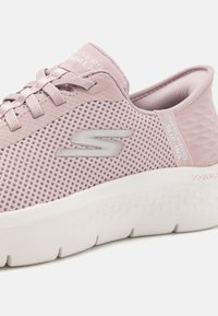 Vaaleanpunaiset Skechers-liukupohjakengät, joissa on verkkokangasta, valkea pehmustettu pohja, nauhat ja logo sivussa.