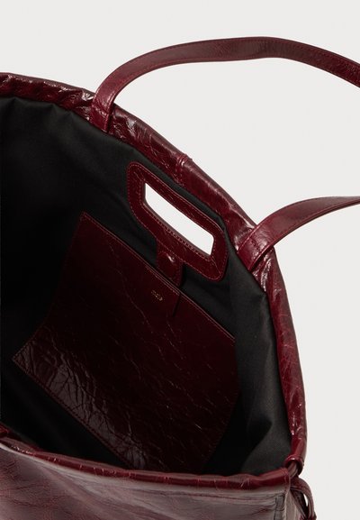 Sac cabas en cuir bordeaux ouvert montrant une doublure intérieure noire et une pochette assortie avec une poignée découpée rectangulaire.