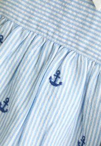 Tessuto a righe blu e bianche con texture arricciata; presenta ancore ricamate in blu navy nella parte inferiore. Morbido cotone.