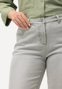 Jeans in denim grigio con un design attillato, dotati di tasca frontale, passanti per cintura e chiusura a bottone metallico. Texture liscia con un leggero luccichio.