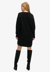 Vestido de suéter negro de gran tamaño, hecho de una tela suave y texturizada, con mangas largas, escote redondo y un corte holgado que llega a la mitad del muslo.