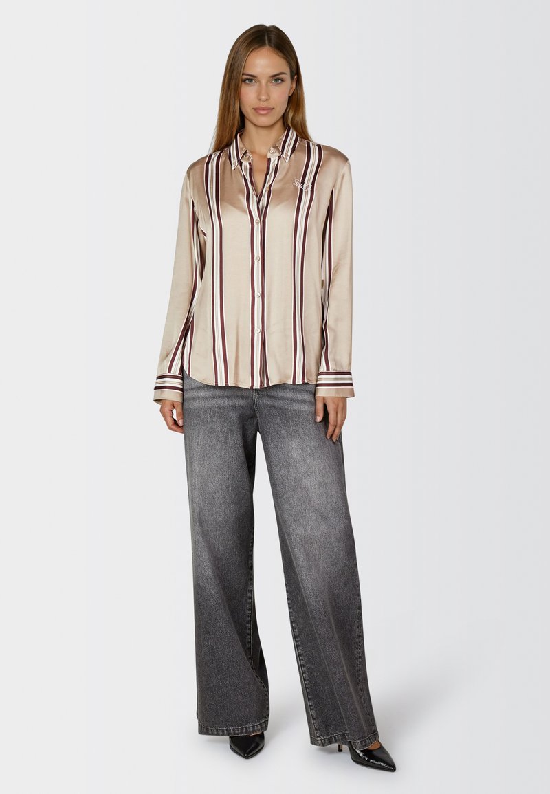 Beige satin shirt with vertical maroon stripes, button-down front, and long sleeves, paired with wide-leg faded gray jeans and black heels.