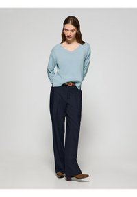 Maglione azzurro chiaro a V, vestibilità rilassata, abbinato a pantaloni navy a gamba larga. Una cintura marrone e stivaletti con tacco marroni completano il look.
