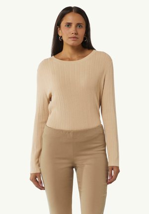 Beige geripptes Langarmoberteil mit weitem Ausschnitt, kombiniert mit hellbraunen, figurbetonten Hosen. Weiche Textur und neutrale Farbtöne.