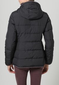 Svart pufferjacka med horisontella sömmar, huva och mjuk yta. Har en figurnära passform och elastiska manschetter. Bakifrån vy visas.