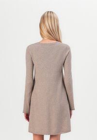 Robe beige à manches longues, avec décolleté rond et jupe évasée. Tissu en tricot doux avec une texture lisse. Pas de motifs ni d'accents visibles.