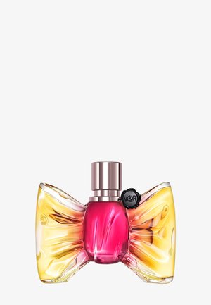Perfume bottle shaped like a bow with yellow glass wings and a pink center, capped with a metallic spray top and a black seal tag.