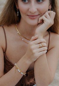 Kullast ja pärlitest ehted hõlmavad kihilist kaelakeed, pärlite ja kettidega käevõrusid ning käel olevat tekstuuriga kuldsõrmust.