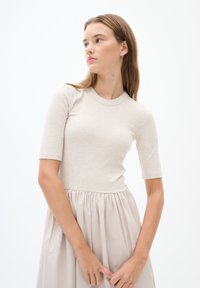 Hellbeige, gerippter Strickoberteil mit kurzen Ärmeln, kombiniert mit einem fließenden, hellbeigen Rock, der an der Taille gerafft ist und so einen weichen Texturkontrast erzeugt.