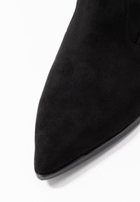 Czarny zamszowy kozak za kostkę z pointed toe i gładkim wykończeniem. Posiada niski, elegancki obcas z minimalnymi akcentami.