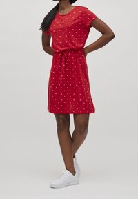 Punaisen lyhythihaisen mekon, jossa on valkoisia pilkkuja, joustava vyötärönauha ja rento istuvuus, yhdistetty valkoisiin tennareihin. Sileä kangas.