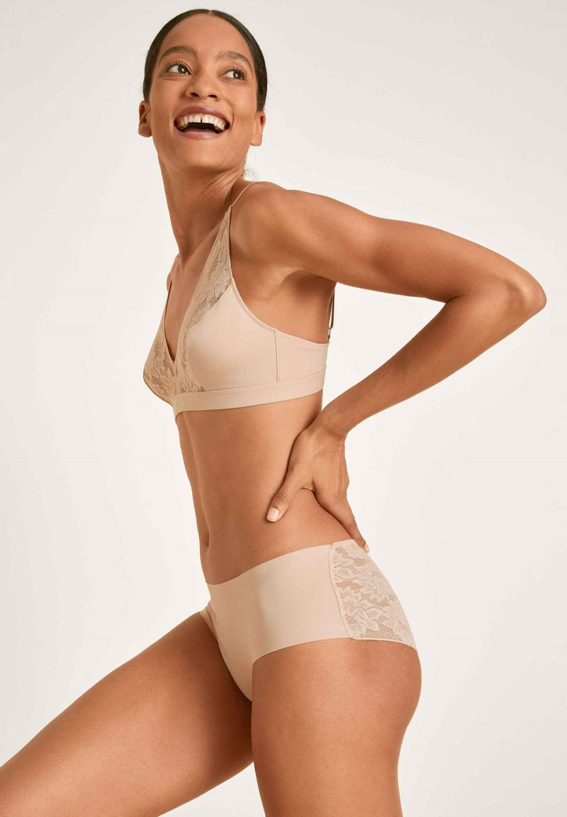 Beige lingerieset met een driehoekige bralette met kantafwerking en bijpassende onderbroek met een kantaccent aan de zijkant. Zachte textuur.