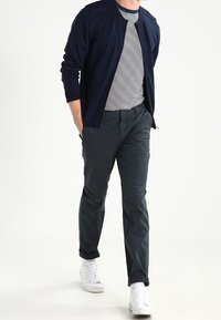 Námořnický svetr přes pruhovanou košili, šedé kalhoty a bílé tenisky. Tento outfit má uvolněný střih a jemnou texturu s minimálními detaily.