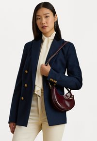 Tumesinine bleiser kuldsete nööpidega, must krae ja kreemivärvi kaelakott; kombineeritud burgundi nahast käekotiga; mudel kannab kreemivärvi pükse.