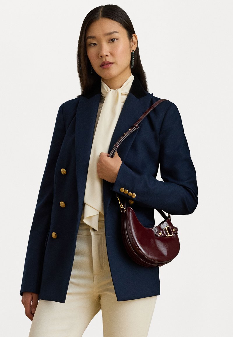 Tumesinine bleiser kuldsete nööpidega, must krae ja kreemivärvi kaelakott; kombineeritud burgundi nahast käekotiga; mudel kannab kreemivärvi pükse.