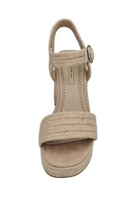 Sandale plateforme beige avec une bride tressée, bout ouvert et une sangle de cheville dotée d'une boucle en métal circulaire. Doublure intérieure lisse.