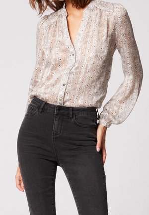 Femme portant un chemisier transparent à manches longues à fleurs, boutonné et rentré dans un jean skinny noir taille haute.