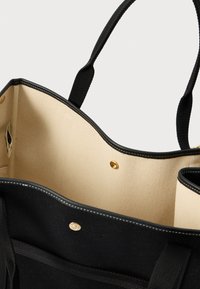 Μαύρη τσάντα ώμου με μπεζ εσωτερικό, μαύρες λαβές και χρυσό κούμπωμα με σnap, που δείχνει την ανοιχτή κορυφή και λεπτομέρειες της εσωτερικής τσέπης.