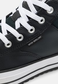 Baskets noires déperlantes avec des lacets blancs, des œillets argentés, un cuir texturé et une semelle contrastée noire et blanche.