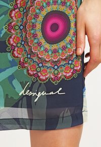 Färgglad design med ett mandala-mönster och blommiga accenter i rosa, grönt och blått. Materialet verkar lättvikts och har en flödande textur.