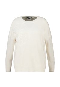 Pull en tricot blanc avec une grande broderie de fleur texturée sur le devant et des détails subtils sur une manche.