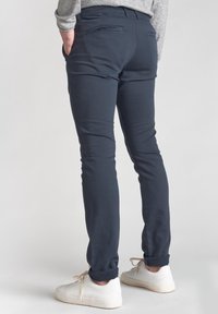 Pantaloni blu navy aderenti realizzati in un materiale liscio, con tasche posteriori e orli arrotolati, abbinati a sneakers bianche.