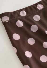 Tissu marron à pois roses, avec une texture lisse et un bord cousu. Le motif est uniformément réparti sur toute la surface.