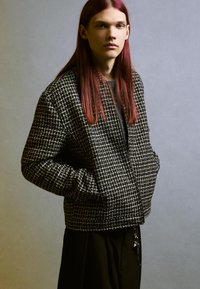 Czarna i biała kurtka w wzory o strukturalnym fasonie, z zamkiem błyskawicznym z przodu i kieszeniami po bokach. Gładki materiał o teksturowanym wykończeniu.