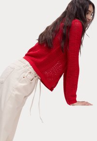 Maglione rosso lavorato a maglia con una vestibilità ampia, caratterizzato da un design testurizzato e maniche lunghe. Abbinato a pantaloni beige chiaro con vita alta.