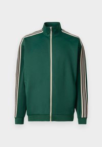 Veste zippée vert en tissu doux et texturé. Présente des rayures blanches et noires le long des manches et un col haut.
