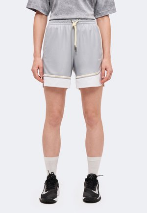 Modèle portant un short de sport gris clair avec des bordures blanches et un cordon de serrage à la taille, des chaussettes blanches et des baskets noires.