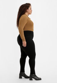 Jeans negros de cintura alta combinados con un top marrón ajustado y acanalado, junto con botas de tobillo. Botones visibles y detalles de tejido texturizado.