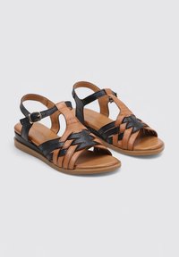 Sandalias de cuero marrón y negro con diseño trenzado, correa ajustable en el tobillo, suela plana y punta abierta. Adecuadas para uso casual.
