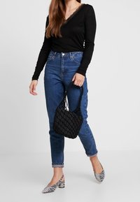 Černý top s dlouhým rukávem a krajkovými detaily, modré džíny s vysokým pasem, černá pletená kabelka a černobílé lodičky s hadím vzorem.