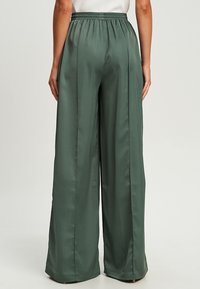 Wijduitlopende broek in een gedempt groene satijnen stof. Voorzien van een elastische tailleband en een soepele textuur; minimale stikdetails zichtbaar.