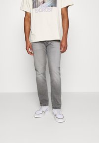 Lichtgrijze jeans met een slim fit, met subtiele vervaging. Gecombineerd met een crèmekleurig graphic t-shirt en witte sneakers.