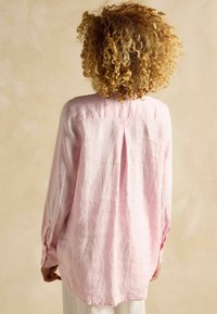 Roosa linane pikkade varrukatega särk, millel on kerge läige, nööpidega mansetid ja voldi detail taga, neutraalse taustaga.