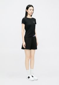 Mustad lühikeste varrukatega T-särk logoga, sobitatud mustade lühikeste pükstega, millel on lilla vöökoht. Valged spordijalatsid mustade detailidega lõpetavad rõivakomplekti.