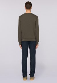 Olivgrön sweatshirt med en enkel design, ribbade ärmslut och nederkant. Bärs med mörkblå jeans och beige skor, sedd bakifrån.