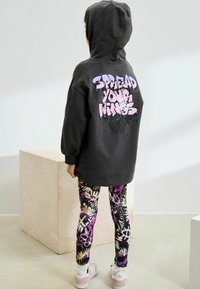 Un sweat à capuche noir avec un texte graphique rose dans le dos, associé à des leggings à motifs multicolores. Des baskets blanches avec des accents.