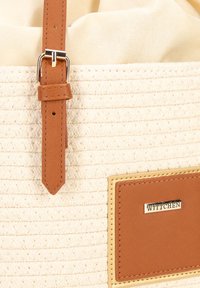 Borsa a tracolla intrecciata beige con una tracolla in pelle marrone, un accento dorato e una patch con logo visibile. Interno in tessuto morbido, forma strutturata.