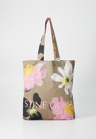 Braune Tragetasche mit großen rosa und weißen Blumenmustern, ausgestattet mit dicken Griffen und dem Text "STINE GOYA" in Pink am unteren Rand.