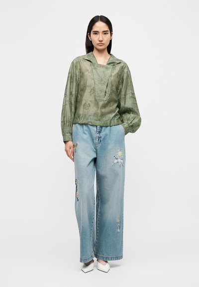 Διάφανη πουκάμισο σε χρώμα ελαιόλαδο με φλοράλ μοτίβο, φαρδιά μανίκια, συνδυασμένο με ανοιχτό μπλε τζιν παντελόνι με κεντημένες λεπτομέρειες και ελαφριά φθορά.