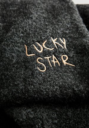 Černá texturovaná látka s výrazným vyšitým nápisem "LUCKY STAR" světle hnědým vláknem, zobrazující měkký, chlupatý povrch.