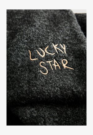 Černá texturovaná látka s výrazným vyšitým nápisem "LUCKY STAR" světle hnědým vláknem, zobrazující měkký, chlupatý povrch.