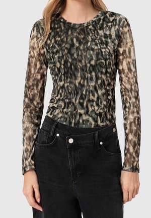 Kvinde iført en langærmet, gennemsigtig top med dyreprint og sorte højtaljede jeans med knap og forlommer.